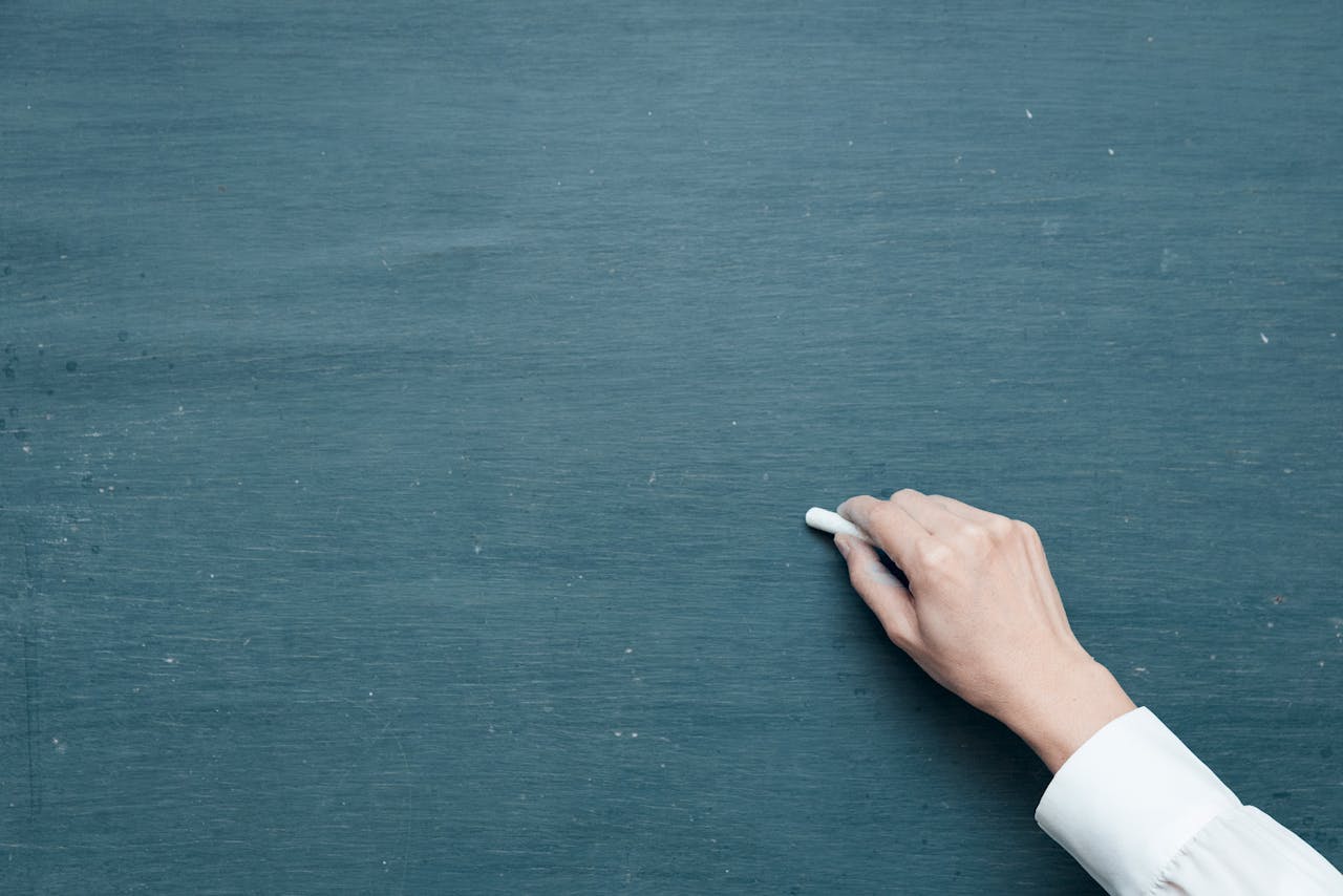 social-feed-img-02 Hand holding chalk ready to write on a blank blackboard surface.